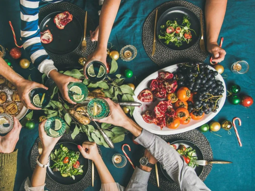 Friends sharing drinks with lemon slices, salads and a platter with fresh fruits