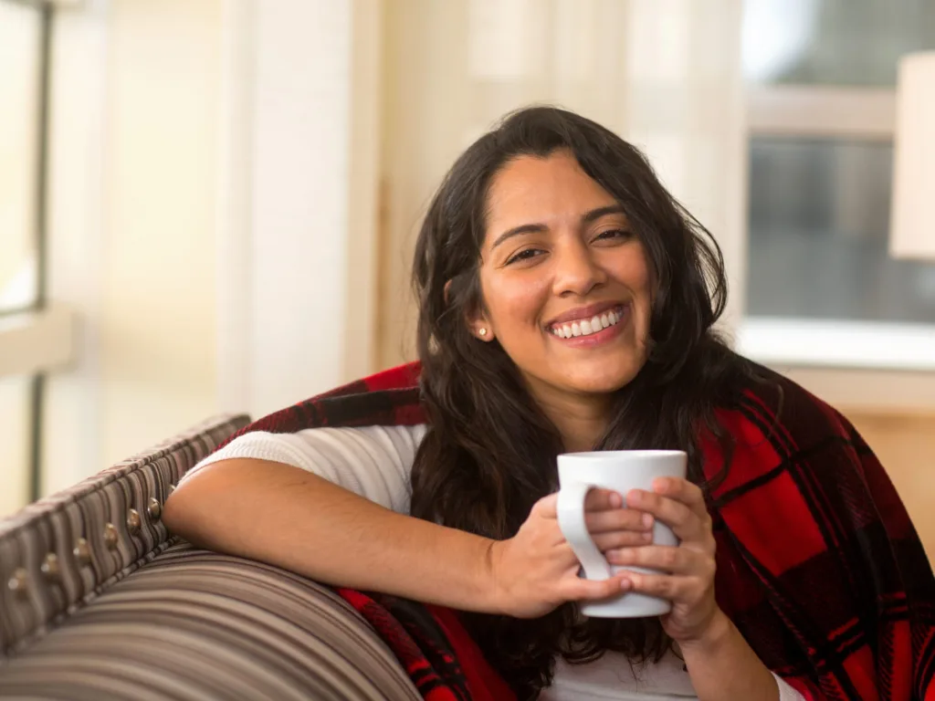 Smiling young woman enjoying a cup of coffee wearing a warm shawl