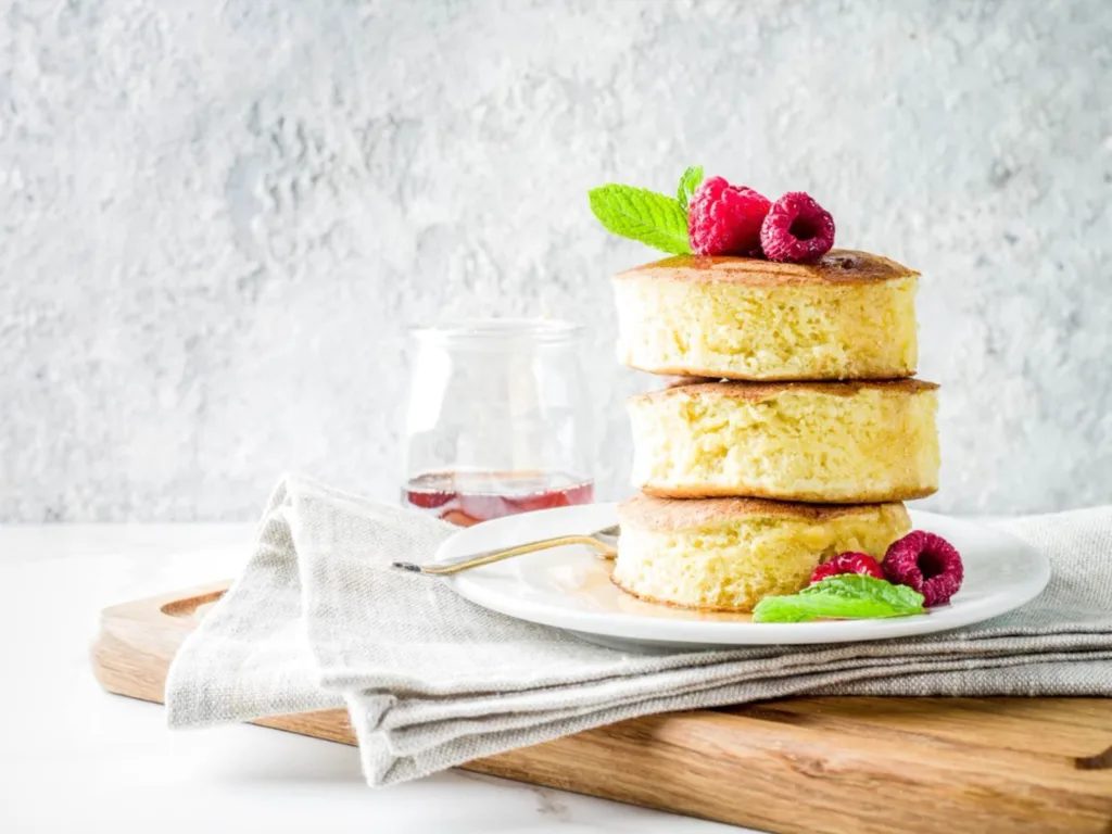 Stack of delicious, fluffy pancakes decorated with raspberries and mint leaves on a plate